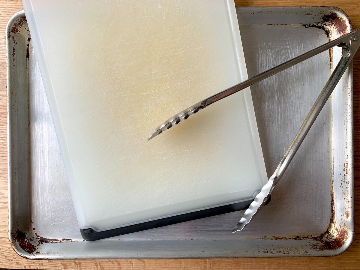 Plastic cutting board, rimmed baking sheet and metal tongs.