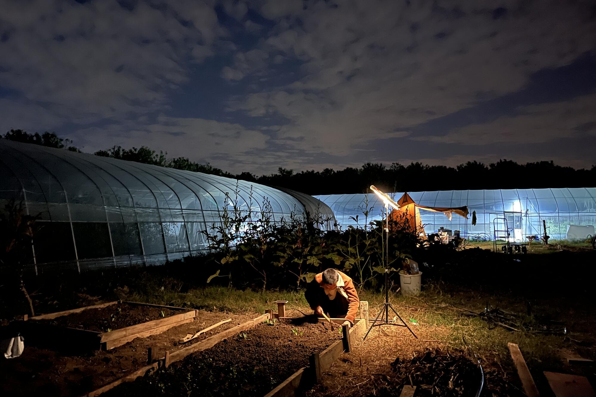 Two people working near greenhouses, illuminated in the dark