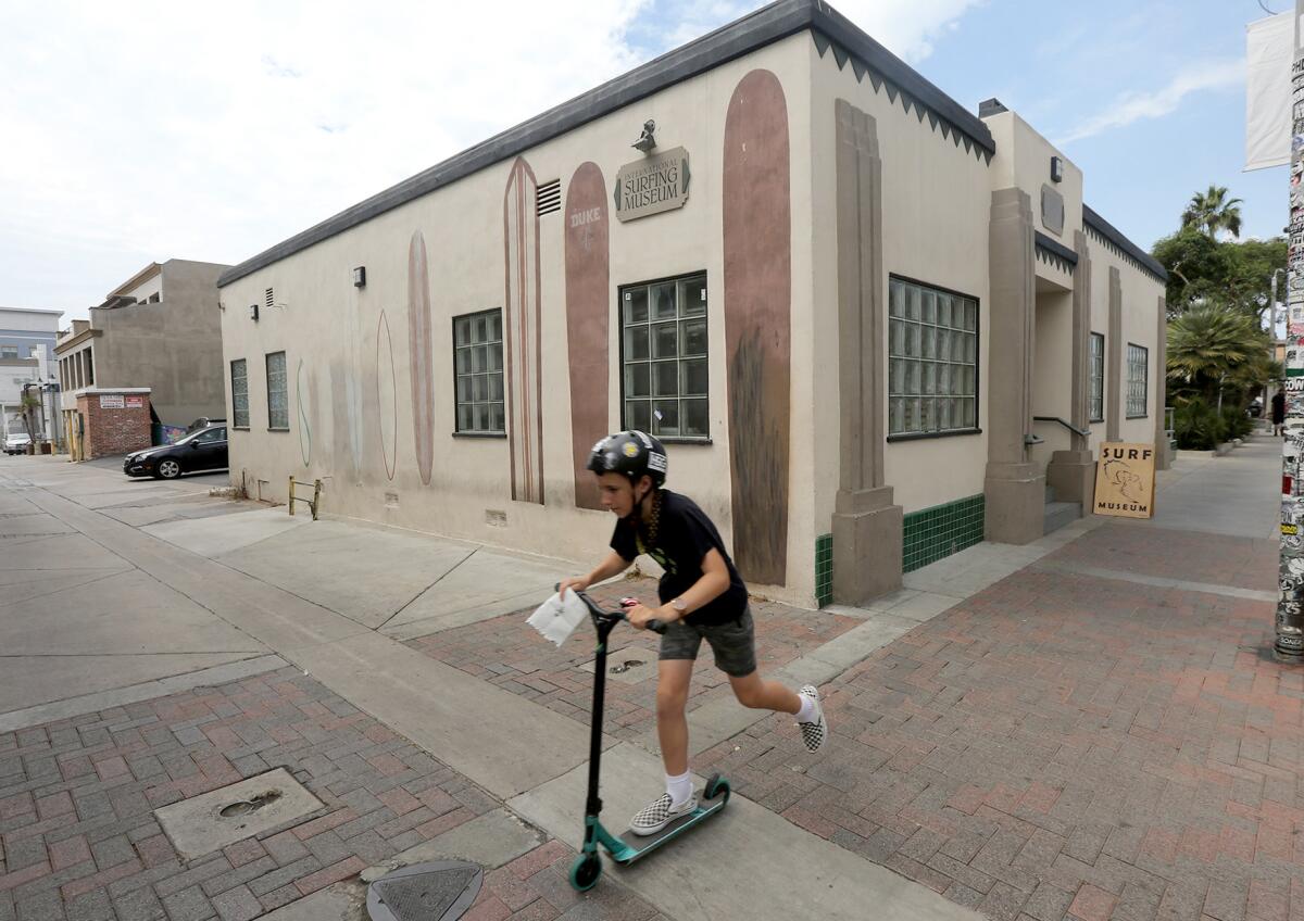 A youngster skates by on a scooter past the International Surfing Museum in downtown Huntington Beach on Thursday.