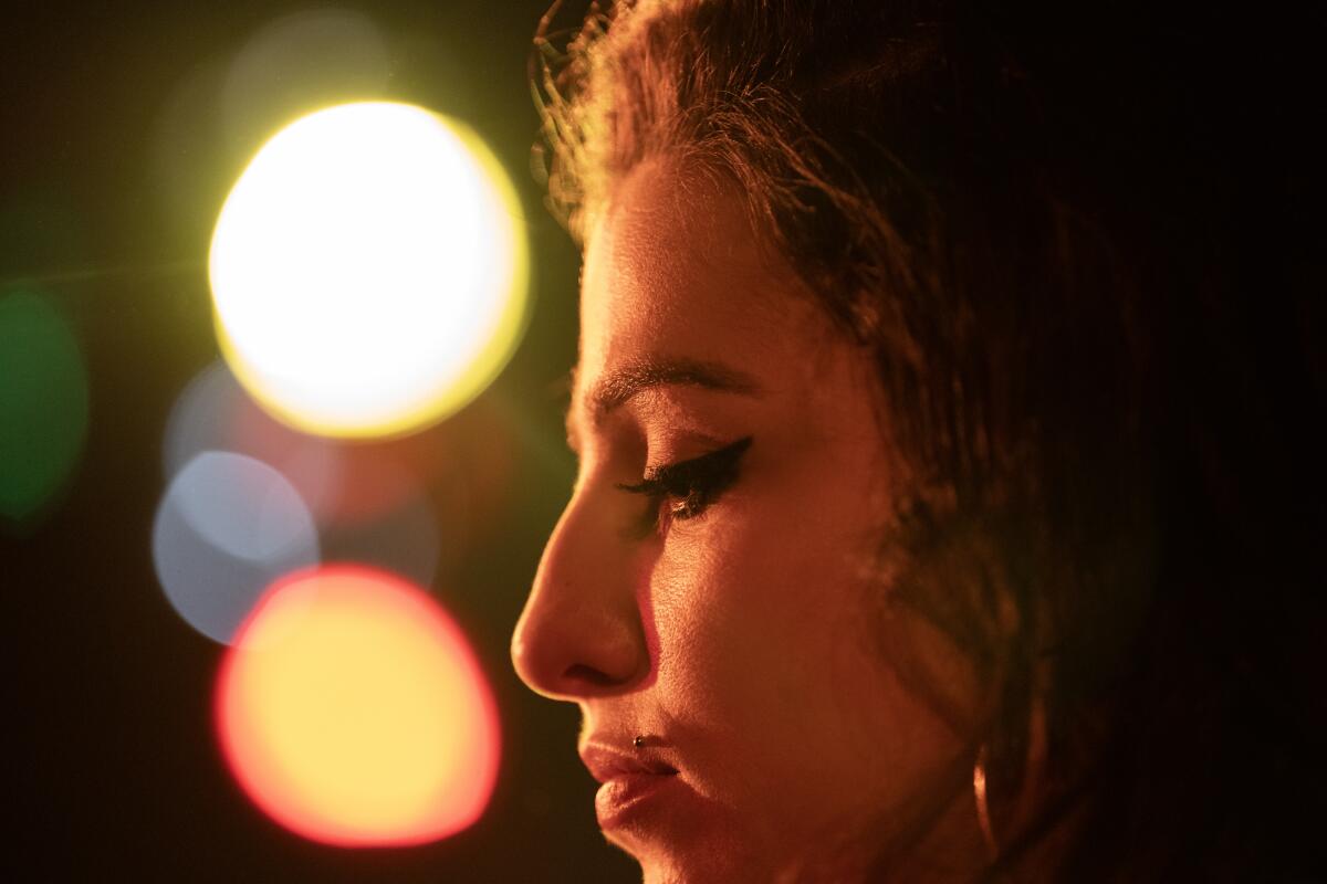 A close-up, profile shot of Marisa Abela as Amy Winehouse, stage lights glowing in the background