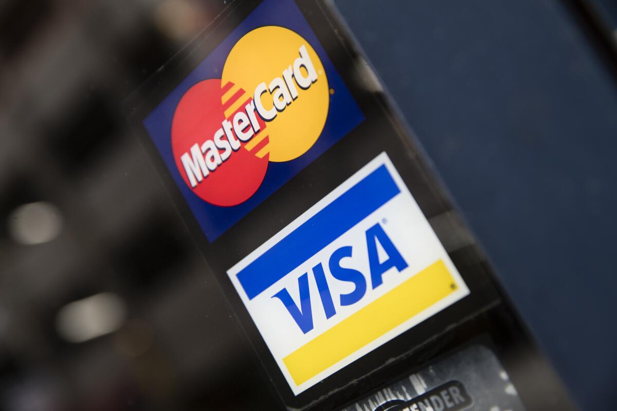 FILE- This Nov. 29, 2018, file photo shows credit card logos posted on a store's door in Philadelphia. The coronavirus pandemic hasnt stopped Americans from keeping up with their credit card payments, thanks in large part to government relief programs passed by Congress earlier this year. For some, however, the ability to keep buying things with plastic and then pay the bill likely depends on whether current negotiations in Washington produce another round of economic aid.(AP Photo/Matt Rourke, File)