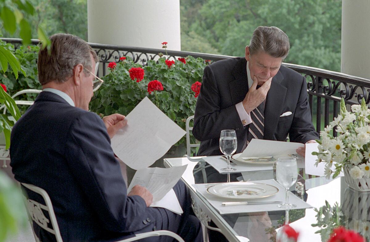 President Reagan, right, and Vice President George H.W. Bush look over papers while sitting at a lunch table.
