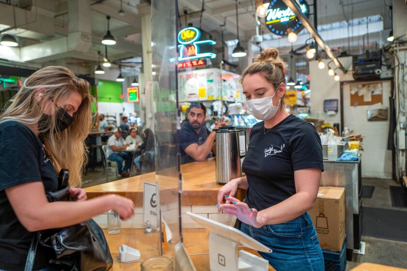 Katelyn Woolcott, right, is continuing to wear a mask as she works at Grand Central Market on Tuesday, March 1, 2022