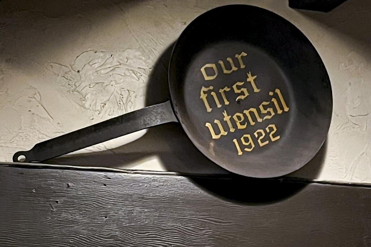 A frying pan mounted on the wall with the words "Our first utensil 1922" written inside.