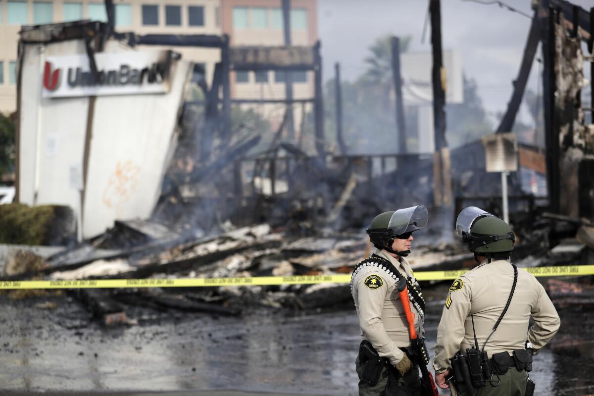 San Diego County sheriff officers stand guard in front of a burning bank building after a protest over George Floyd's death on Sunday in La Mesa, Calif.