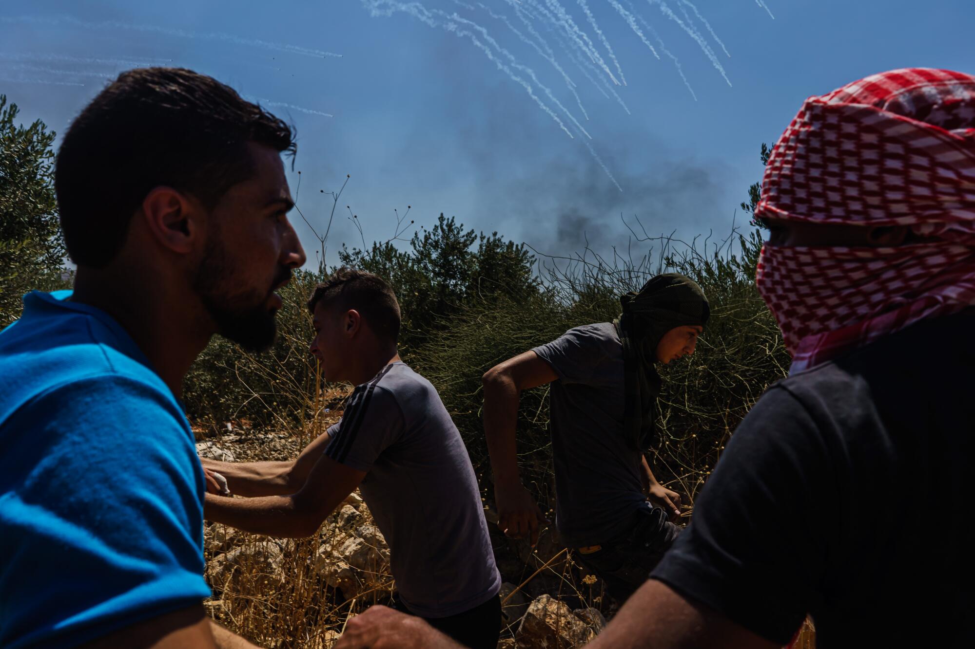 Palestinians run in different directions to avoid tear gas canisters fired by Israeli forces during their protest.