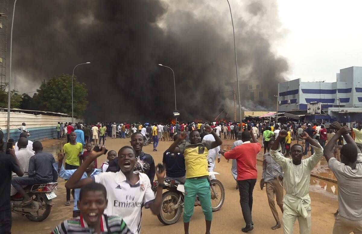 With smoke rising in the background, supporters of mutinous soldiers demonstrate in Niamey, Niger.