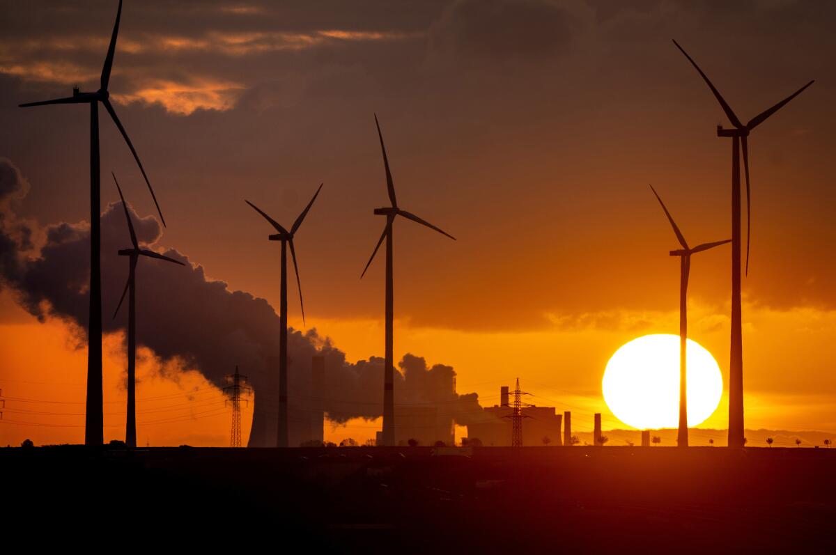 Steam rises from a coal power plant, with wind turbines in the foreground