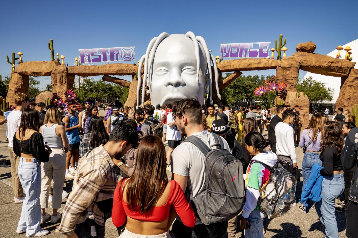 A crowd of people gathers outside a music festival entrance featuring a large head of man with dreadlocks.
