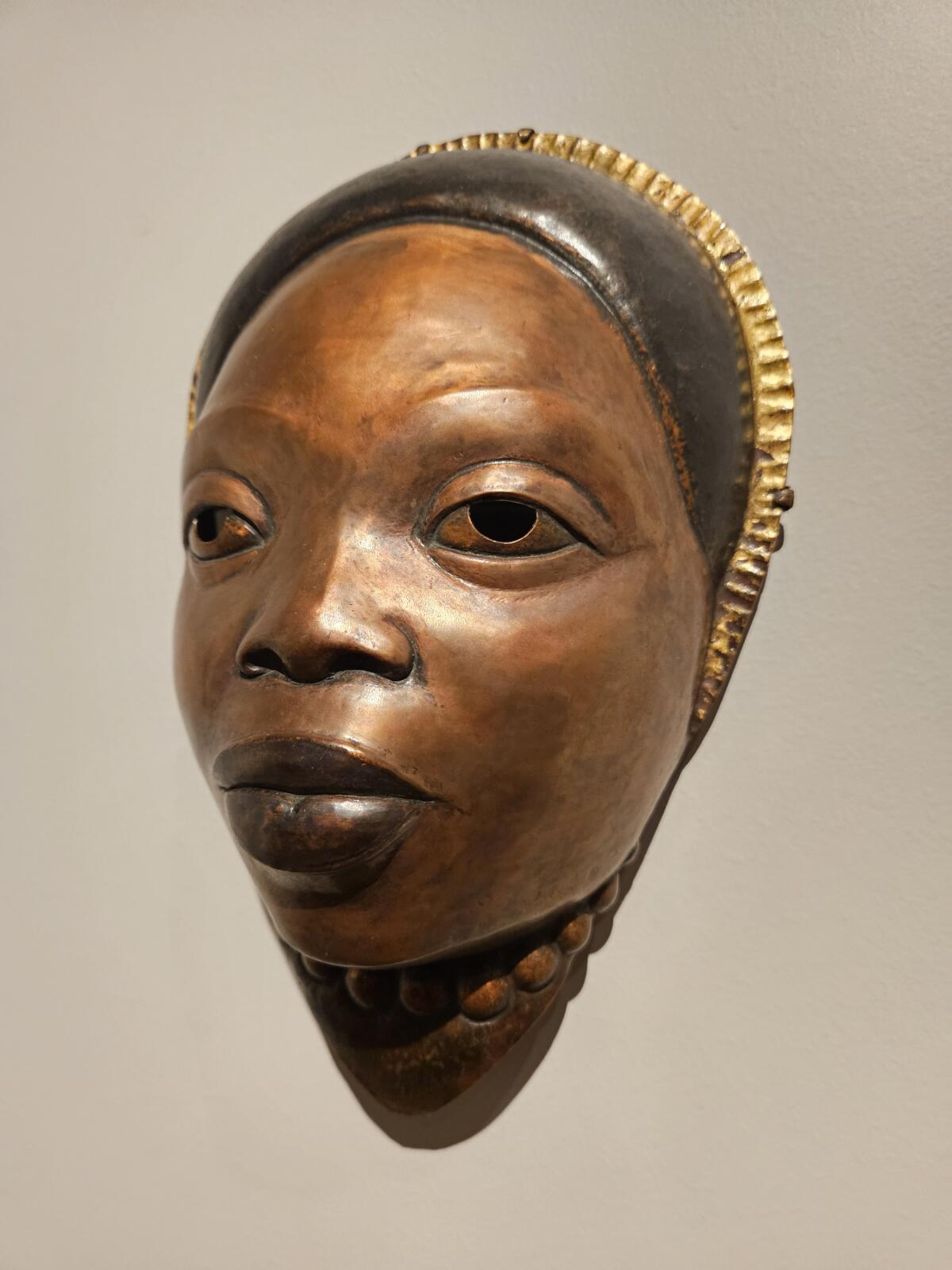 A copper mask of Black mother with a gold headband. 