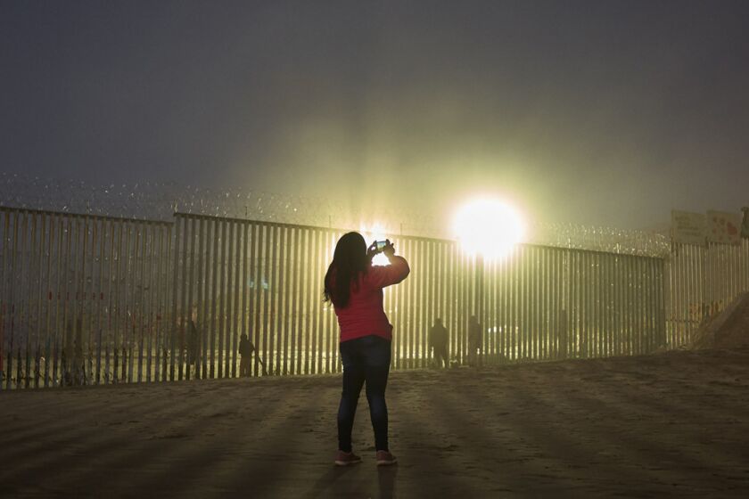 FILE - In this Jan. 10, 2019, file photo, a woman records with her phone, as floodlights from the United States light up the border wall, topped with razor wire along the beach in Tijuana, Mexico. The government is working on replacing and adding fencing in various locations, and Trump in February declared a national emergency to get more funding for the wall. (AP Photo/Gregory Bull, File)