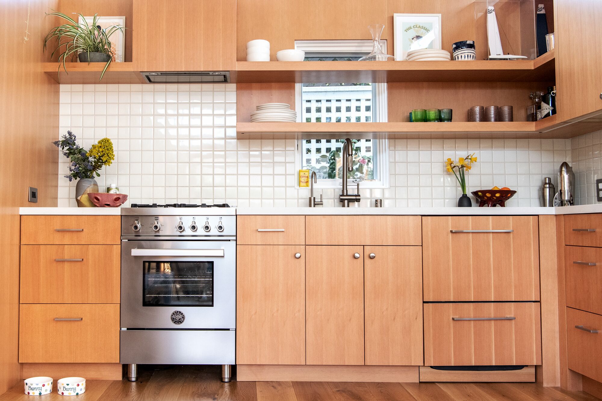 A tiny kitchen with natural wood cabinets and white tile.