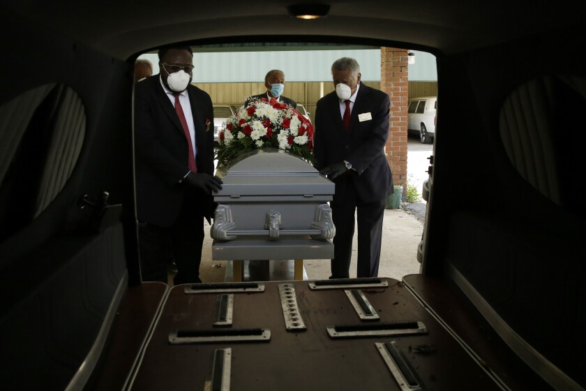 Three pallbearers wearing masks hold a casket.