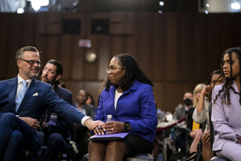 WASHINGTON, CA - MARCH 21: Patrick Jackson, husband of Supreme Court nominee Judge Ketanji Brown Jackson, reaches out to hold her hand as she sits in the audience area with her family during her Senate Judiciary Committee confirmation hearing on Capitol Hill on March 21, 2022 in Washington, DC. Judge Jackson was picked by President Biden to be the first Black woman in United States history to serve on the nation's highest court to succeed Supreme Court Associate Justice Stephen Breyer who is retiring. (Kent Nishimura / Los Angeles Times)