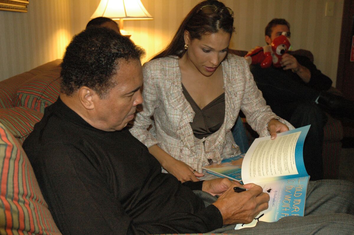 Muhammad Ali sits next to his daughter Rasheda Ali as he signs his name in a copy of her book