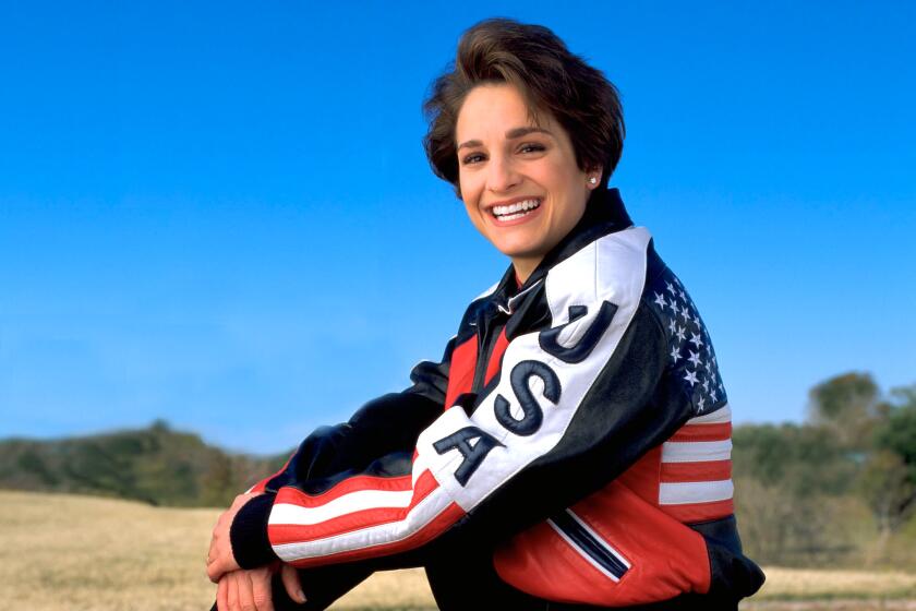 Mary Lou Retton smiles and poses in a U.S.A. tracksuit with bronze, silver and gold medals.