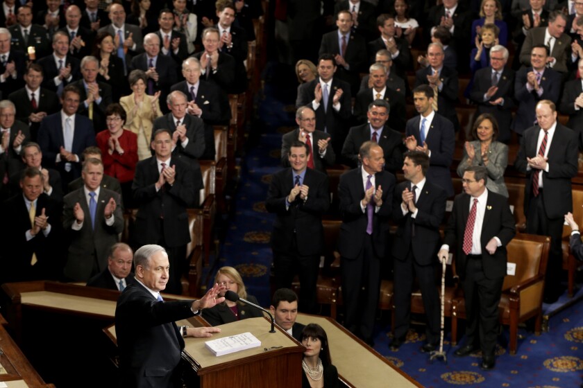 Congress members stand and applaud Benjamin Netanyahu, who stands on a podium.