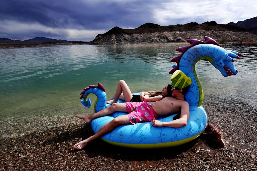 LAKE MEAD, NEV - DEC 24, 2021. Visitors to the Lake Mead National Recreation Area lounge on a toy raft at the edge of the lake, were a "bathtub ring" of white on the surrounding landscape shows how much water levels have dropped in the vast Colorado River reservoir. (Luis Sinco / Los Angeles Times)