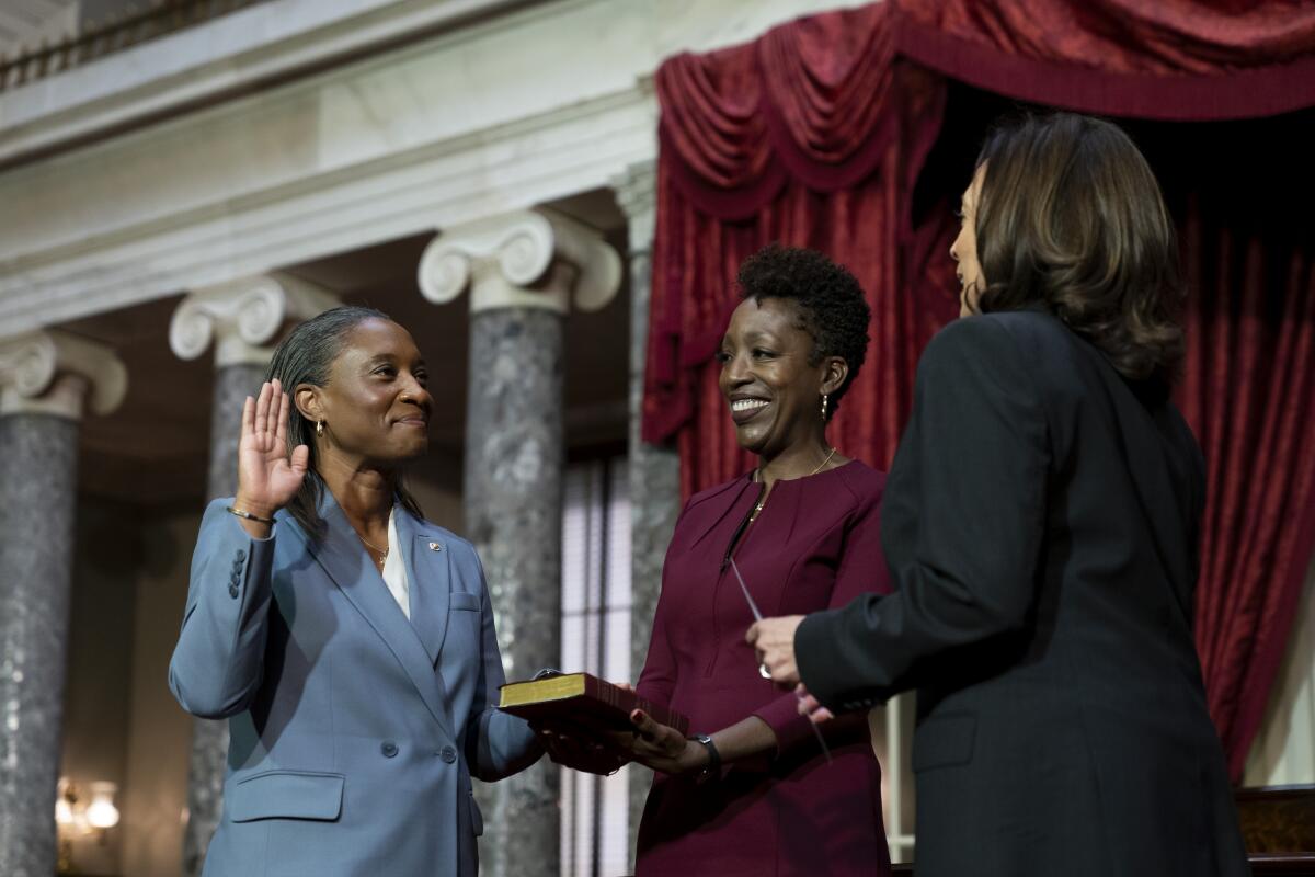 A woman in a blue jacket, left, holds up one hand, with the other on a Bible, facing other two women 