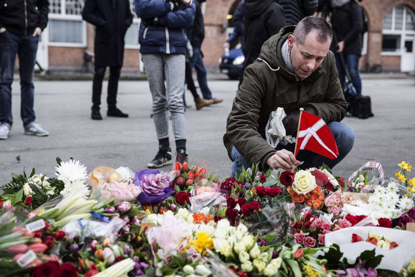 A man places a Danish flag next to flowers for the shooting victims outside the "Kruttoende" cultural centre in Copenhagen.