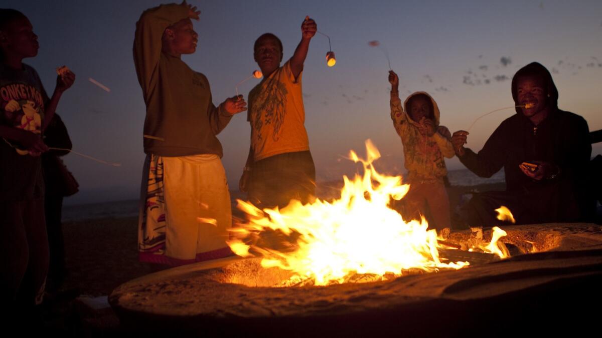 A family roasts marshmallows as members gather around a bonfire pit on Dockweiler State Beach in Playa del Rey.