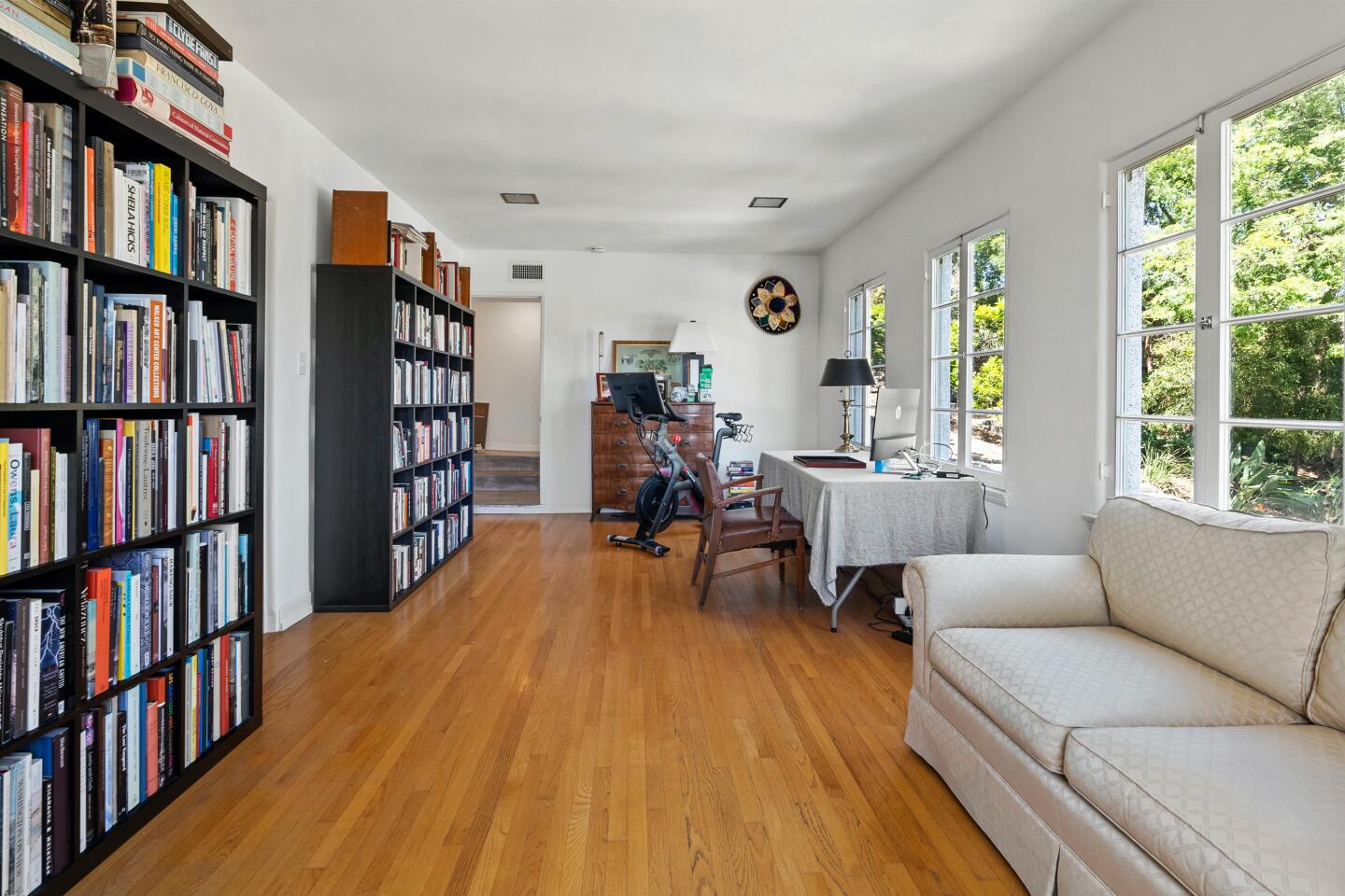 The office with hardwood floor, furniture and book-filled bookcases and windows.