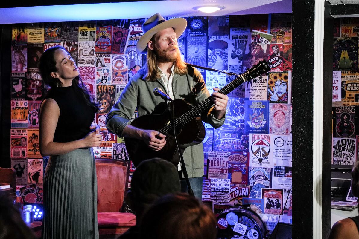 A man plays guitar standing next to a woman singing on a small stage