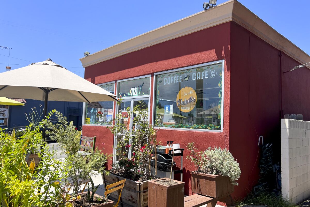 A small reddish building with an outdoor patio featuring wooden planter boxes, tables and chairs.