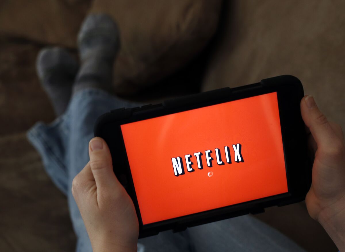 A person lies on a couch holding a tablet displaying the Netflix logo