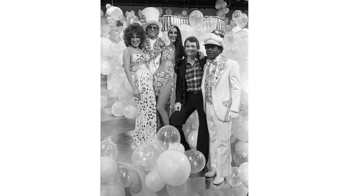 January 1975: Four luminaries wearing designs by Bob Mackie take a break with the designer during taping of "The Cher Show." From left: Bette Midler, Elton John, Cher, Bob Mackie and Flip Wilson.