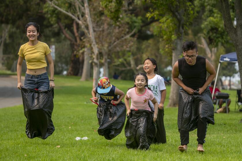 FOUNTAIN VALLEY, CA - SEPTEMBER 07: From left, Annie Nguyen, 17, Jordan Cheung, 7, Kendra Cheung, 8, Katelyn Le, 9, Phu Le, 17, have a family sack race; one of many family games they played together while picnicking as hundreds of people spread out over Mile Square Park to celebrate Labor Day with their families and got relief from the heat wave Monday, Sept. 7, 2020 in Fountain Valley. (Allen J. Schaben / Los Angeles Times)