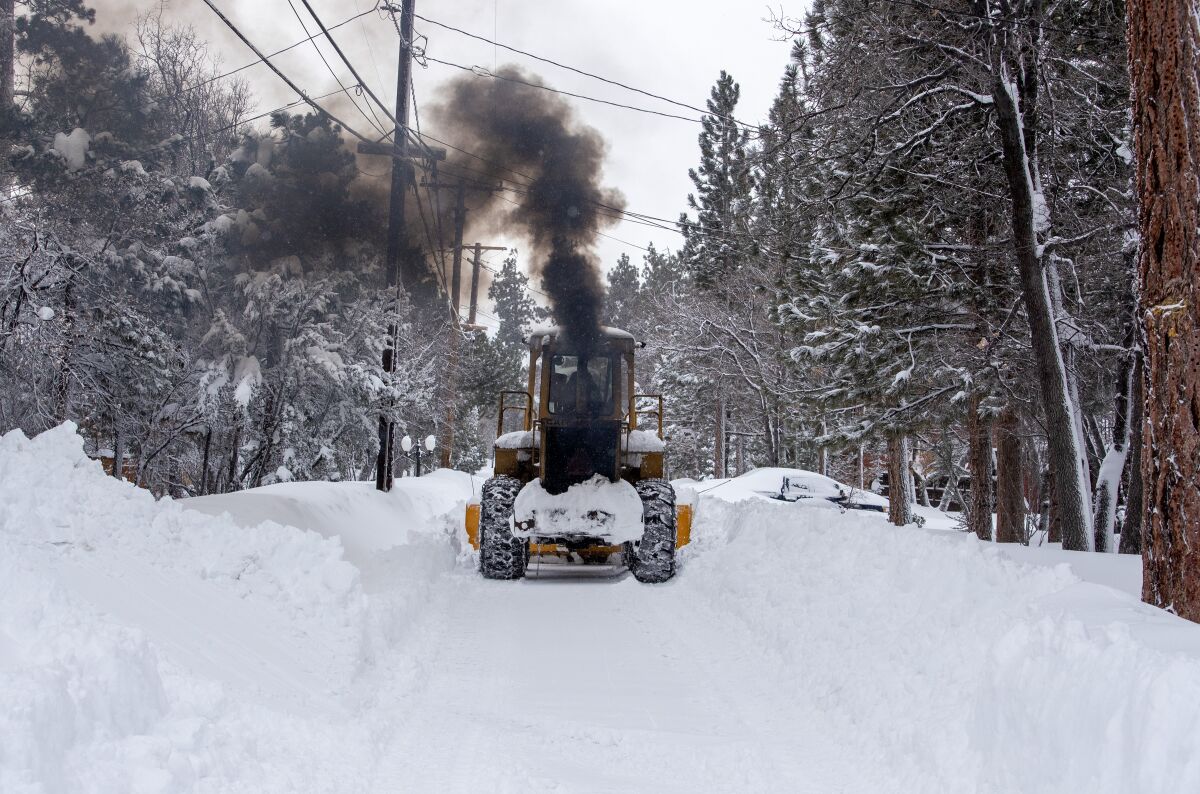 A snowplow belches black smoke as it clears a path past trees covered with snow.
