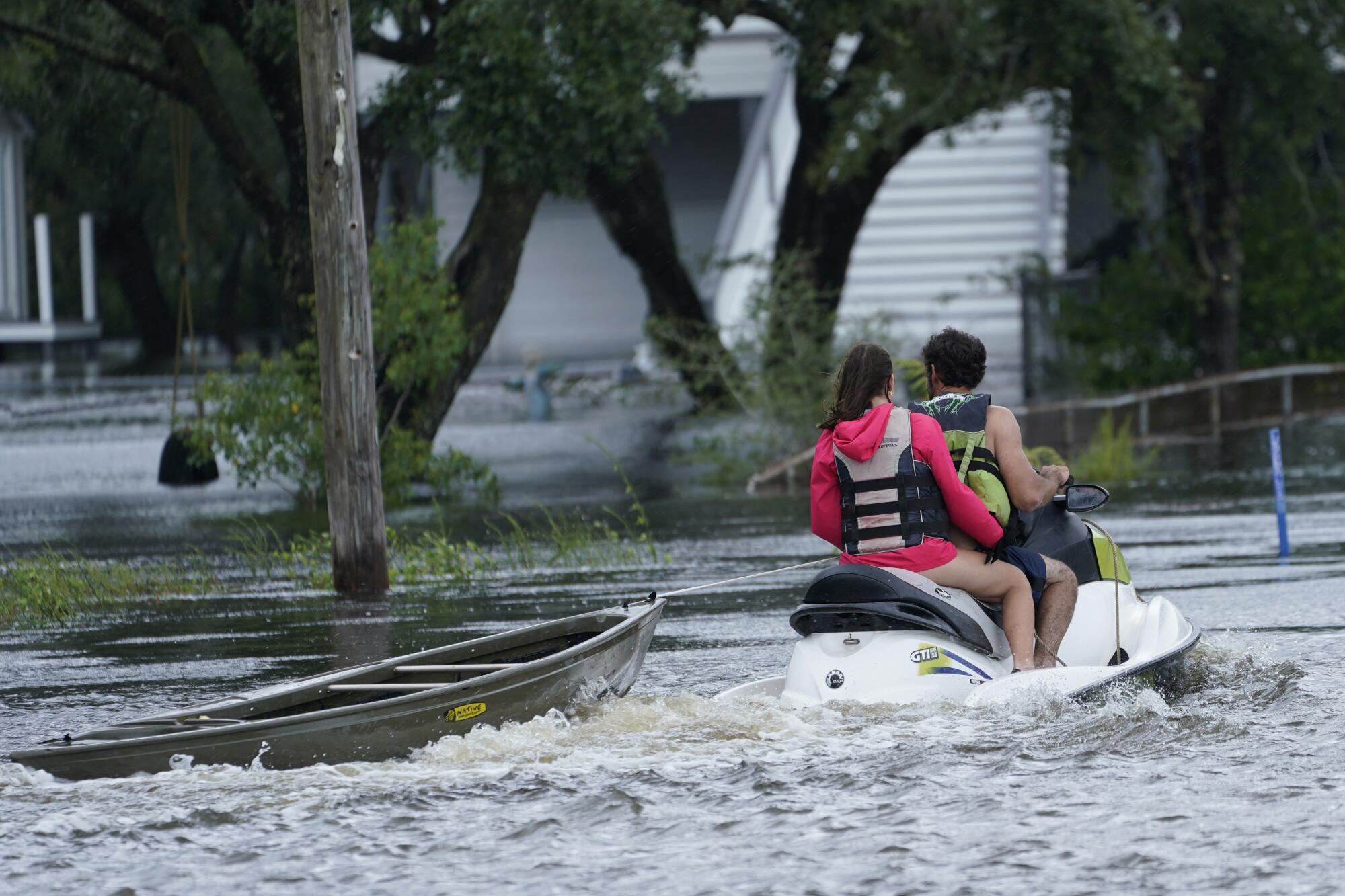 Two people wear life vests on a personal watercraft.