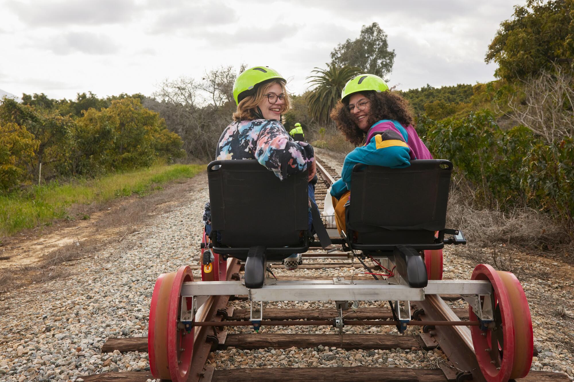 Julia Carmel and Reanna Cruz looking backward from their railbike, smiling at the camera.