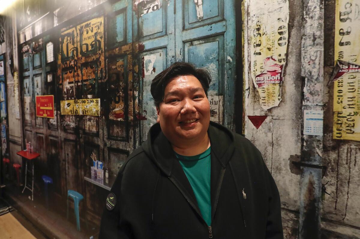 Kanate Ungkasrithongkul stands next to a photographic mural of Bangkok, Thailand.