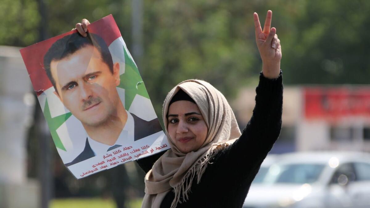 A supporter of Syrian President Bashar Assad waves his portrait as she and other Syrians gather in Damascus on Saturday to condemn the strikes carried out against the Syrian government.