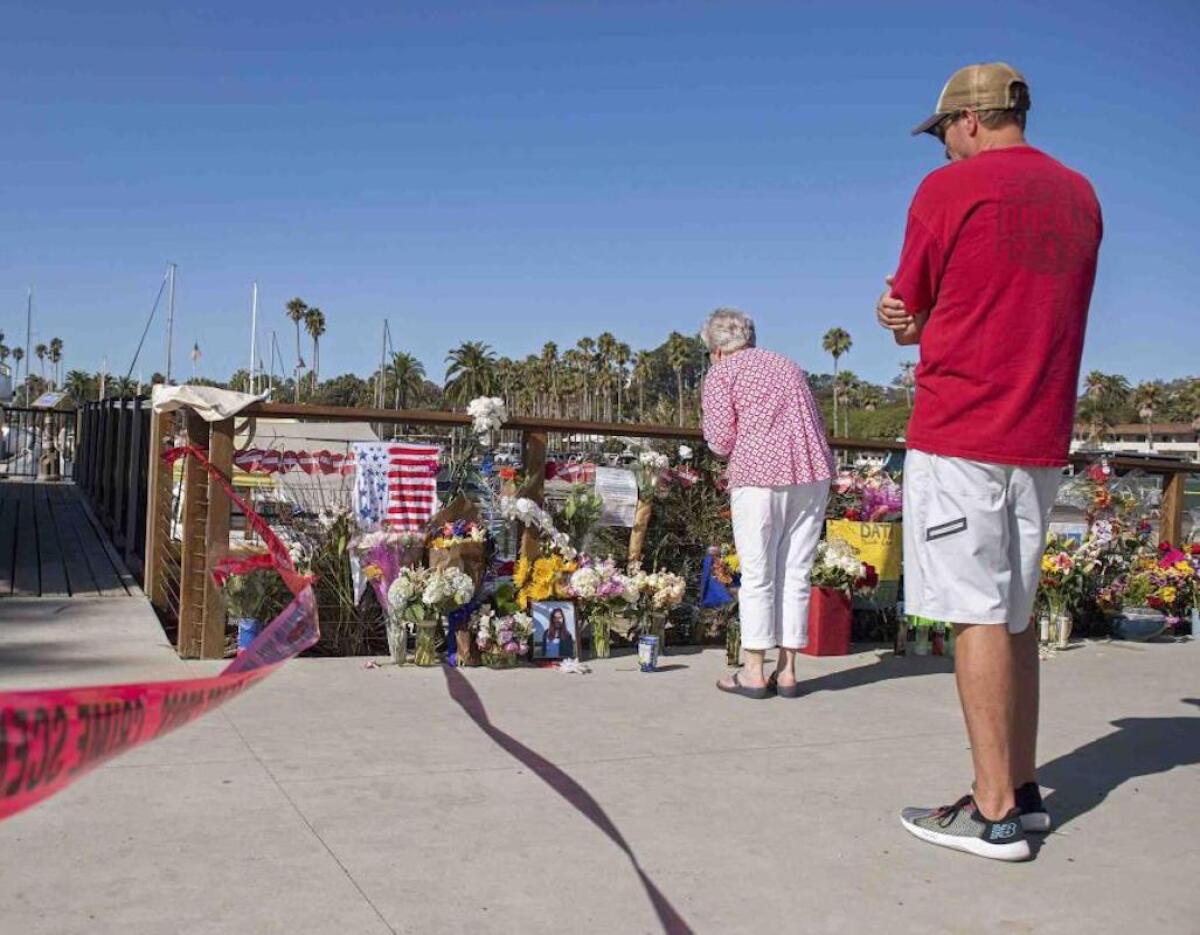 Dos personas observan un monumento conmemorativo improvisado colocado en honor de las víctimas de un incendio en un bote de buceo mientras las autoridades allanaban las oficinas de Truth Aquatics, la compañía propietaria de la embarcación, en Santa Barbara, California.