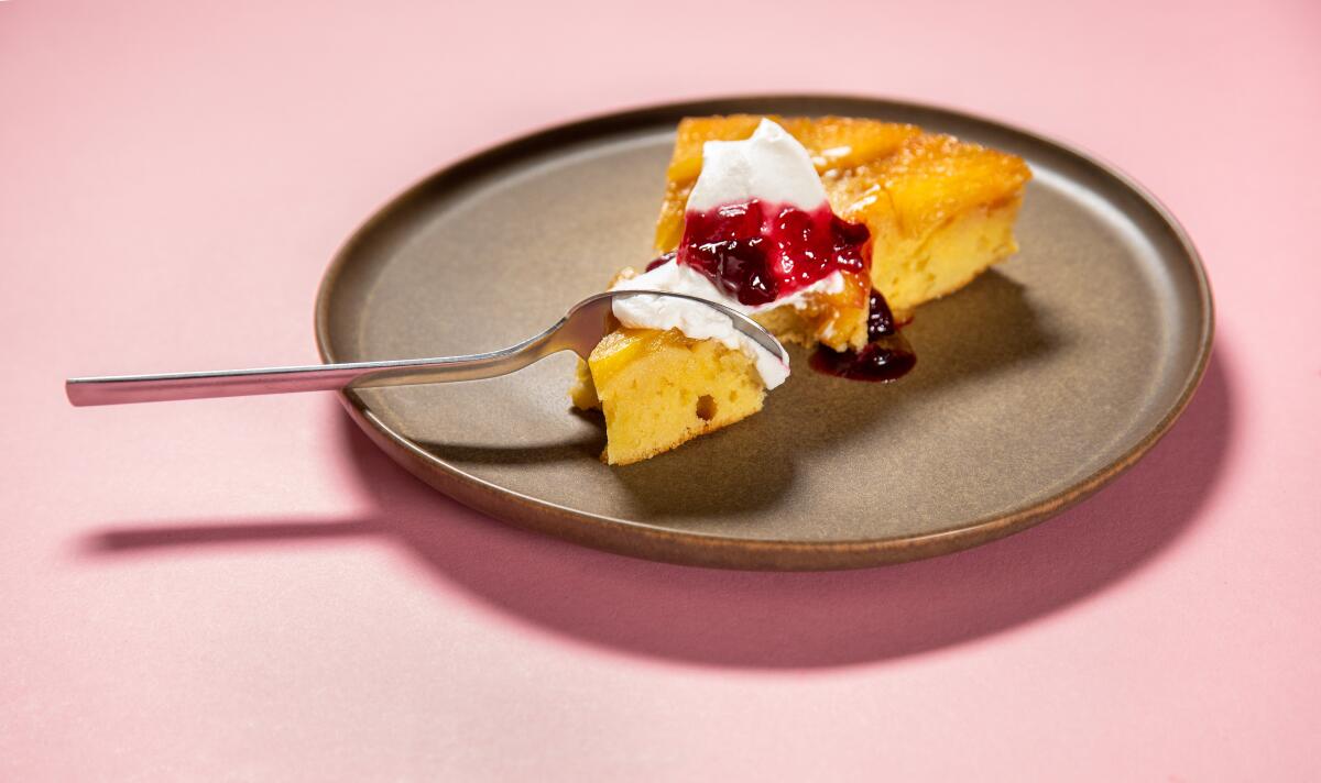 A slice of pineapple upside down cake with whipped cream and cherries on top on a plate