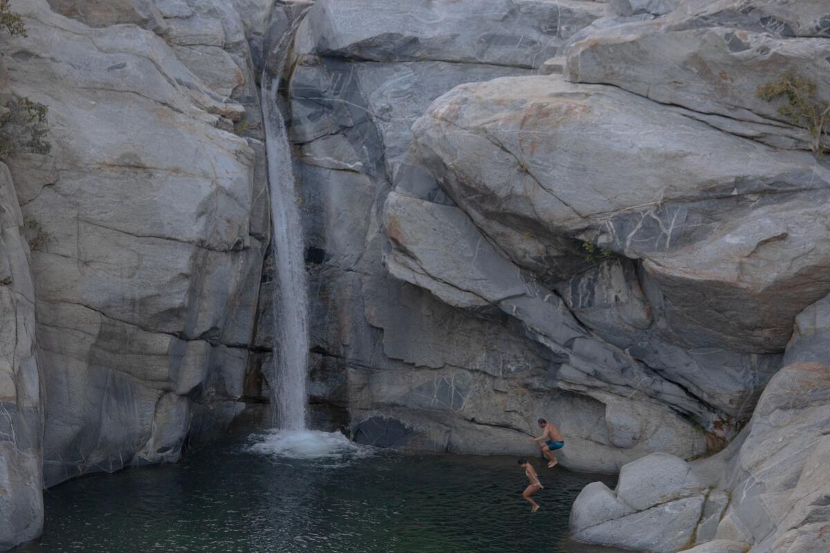 A couple jumping off some rocks into a body of water, with a long waterfall in the background.