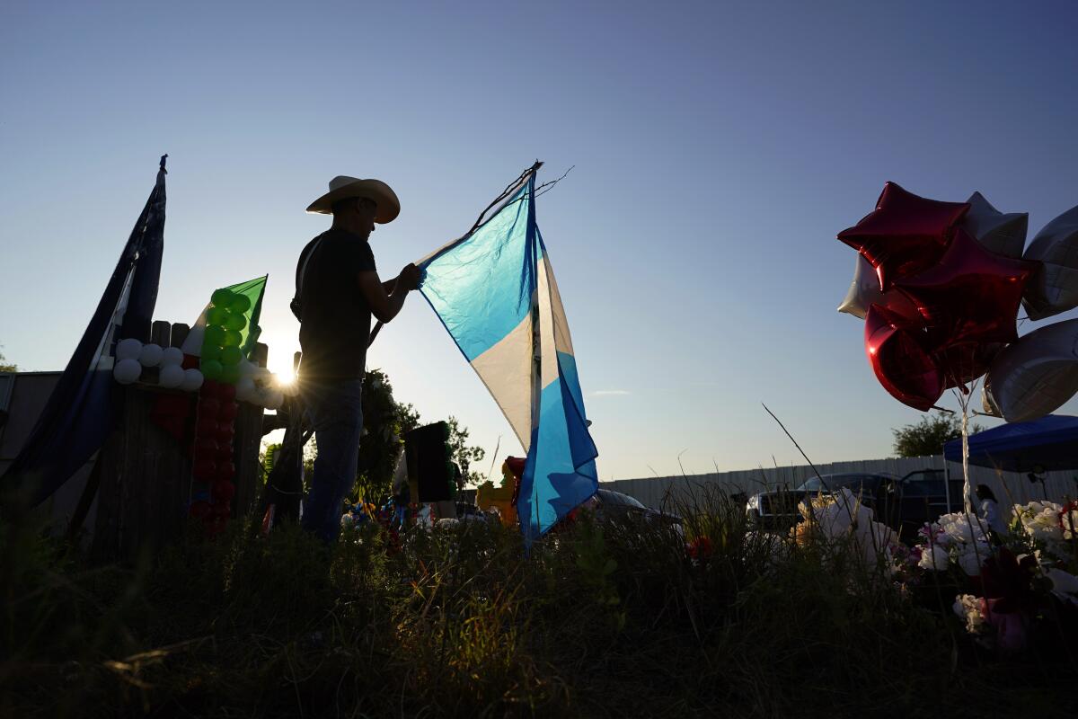 Roberto Marquez adds a Guatemalan flag to a makeshift memorial at the site where officials more than 50 people dead in an abandoned semitrailer containing suspected migrants, Thursday, June 30, 2022, in San Antonio. (AP Photo/Eric Gay)