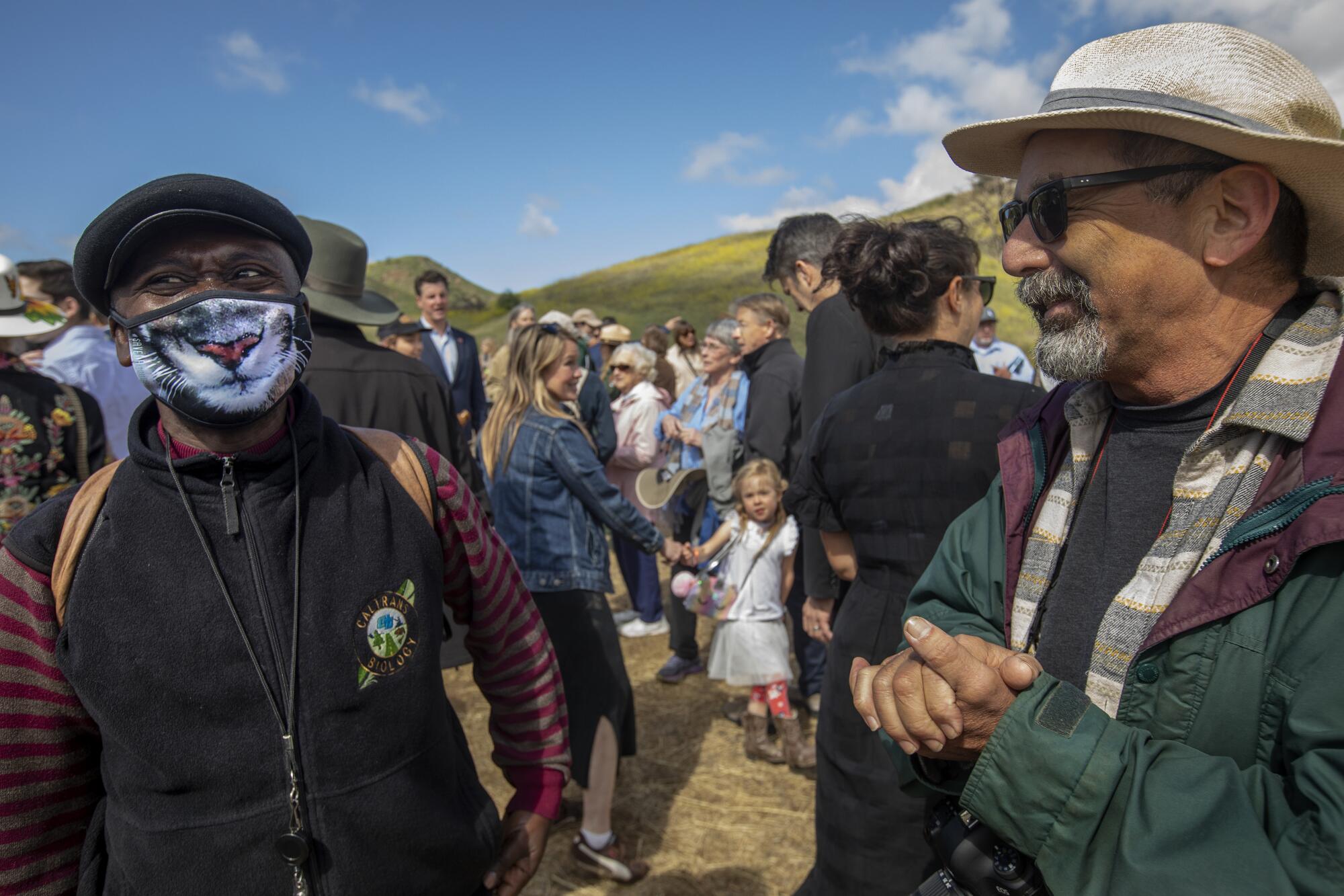 A man wears a face mask that looks like a big cat's nose and mouth while other people stand nearby outdoors.