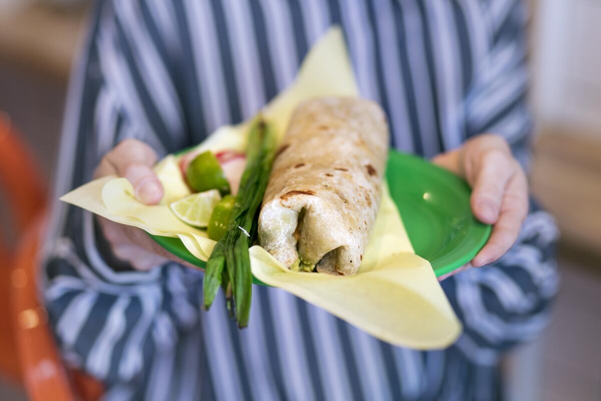 A person holding out a burrito with grilled scallions on a green plate