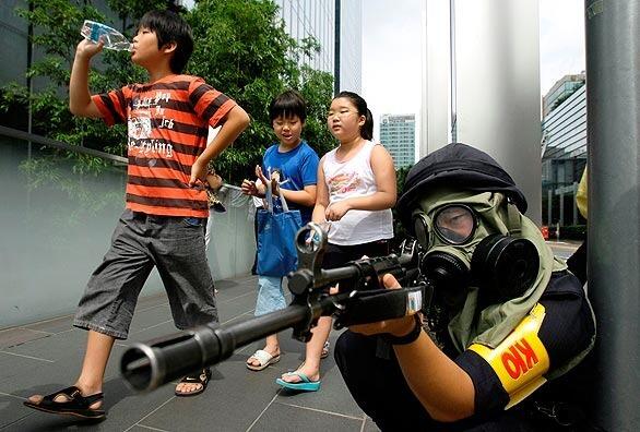 South Korean children walk past as a police officer aims his weapon during an anti-terrorism exercise at the Samsung Electronics building.