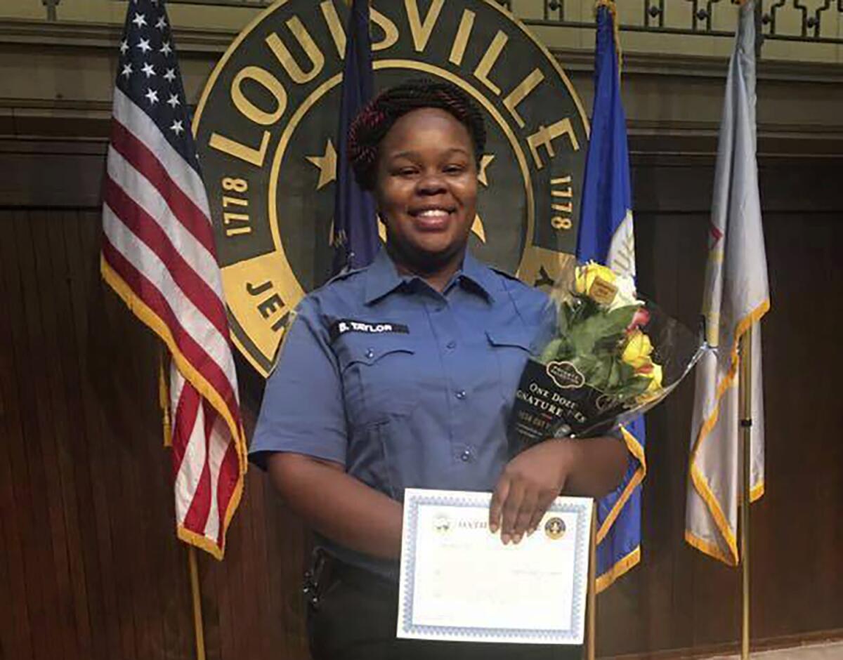 Breonna Taylor smiles while holding a certificate and flowers.