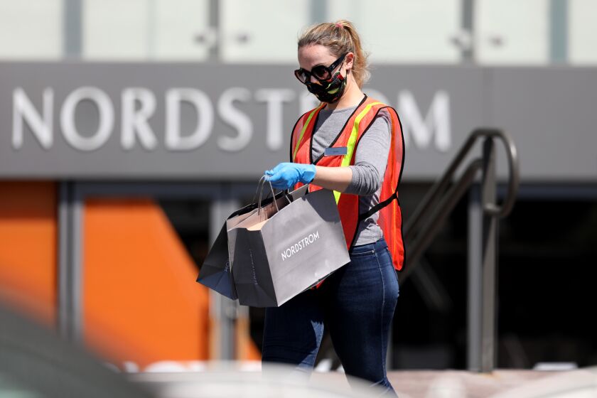 COSTA MESA, CA -- MAY 15: A Nordstrom employee delivers merchandise to a customers waiting in their vehicles at curbside pickup outside Nordstrom at South Coast Plaza on Friday, May 15, 2020, in Costa Mesa, CA. South Coast Plaza has joined the list of outlets offering contact-free pickup for customers amid the coronavirus pandemic. Customers remain in their auto while their items are put in their car's trunk. (Gary Coronado / Los Angeles Times)