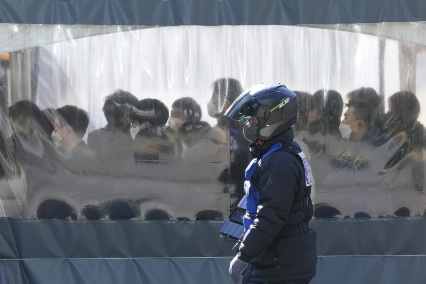 Una persona, con un casco de motocicleta y mascarilla, pasa por delante de un centro temporal de pruebas de detección del coronavirus, en Seúl, Corea del Sur, el 28 de enero de 2022. (AP Foto/Ahn Young-joon)