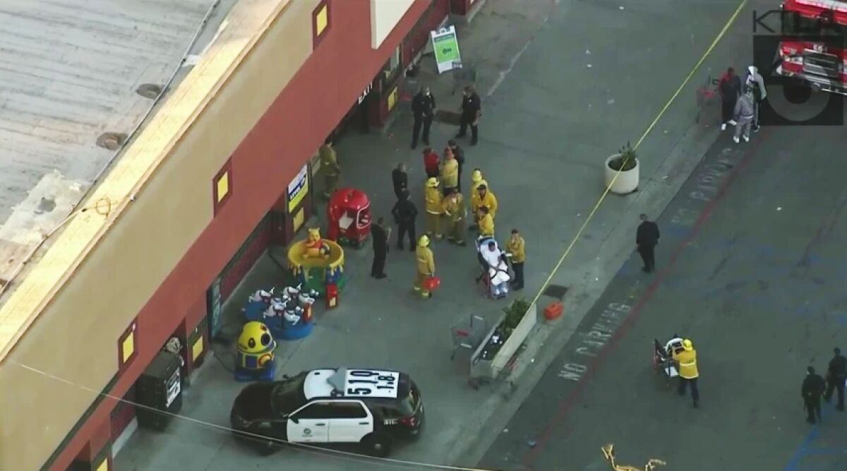Firefighters and police with a patient strapped into a wheelchair at a taped-off crime scene outside a grocery store