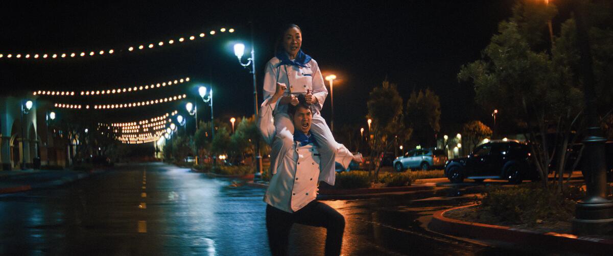 A man in a chef's jacket runs with a woman on his shoulders pulling at his hair to steer him in "Everything Everywhere."