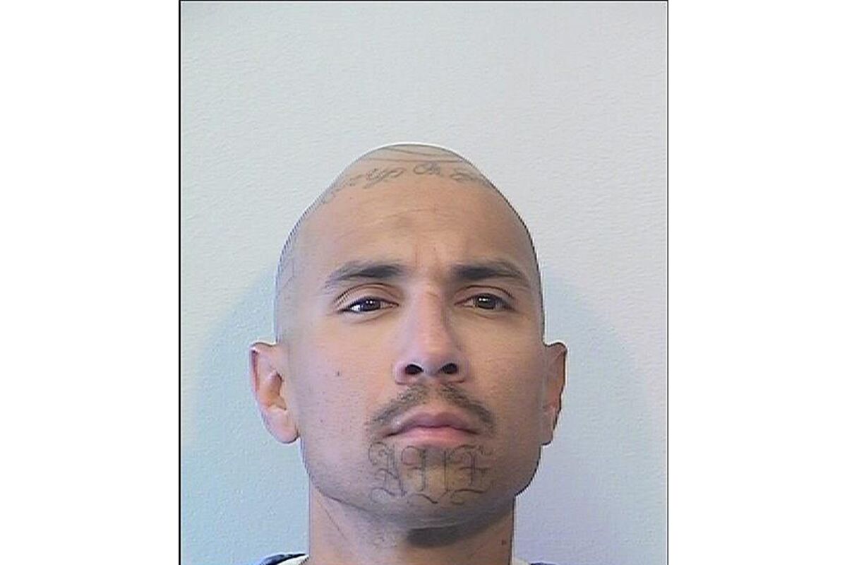 A prison mug shot of a man with tattoos on his chin and on top of his shaved head