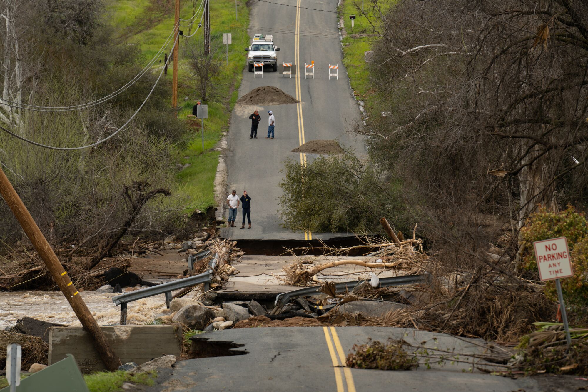 A paved road is washed out.  People stand nearby.